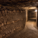 Dark underground tunnel inside the Catacombs of Paris lined with human skulls and bones beneath the streets of France