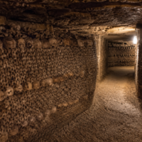 Dark underground tunnel inside the Catacombs of Paris lined with human skulls and bones beneath the streets of France