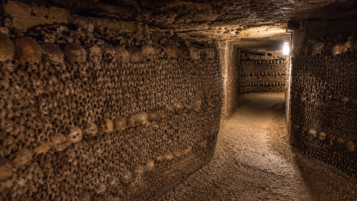 Dark underground tunnel inside the Catacombs of Paris lined with human skulls and bones beneath the streets of France