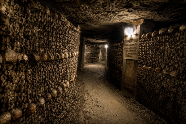 Eerie bone-lined hallway deep inside the Paris Catacombs with dim lighting and ancient stone walls